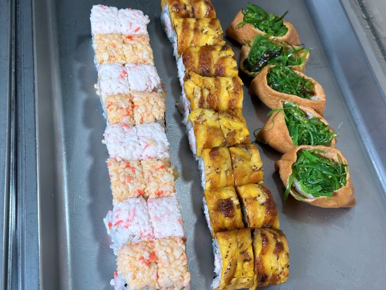 Rows of crab stick rolls, eel rolls and seaweed-salad inari