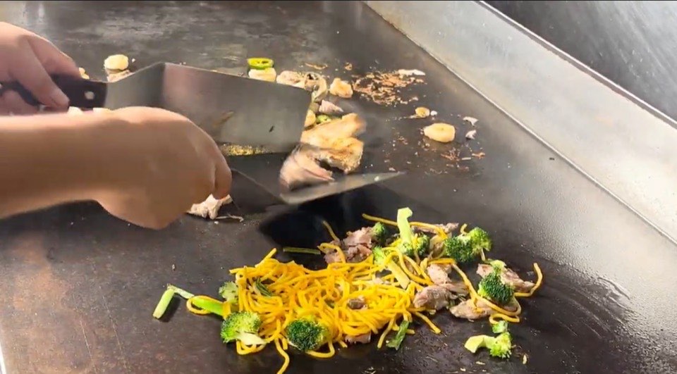 Chef cooking noodles, broccoli and beef on the hibachi grill